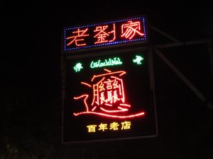 Bowl of biangbiang noodles with chili oil, vegetables, and toppings on a wooden table