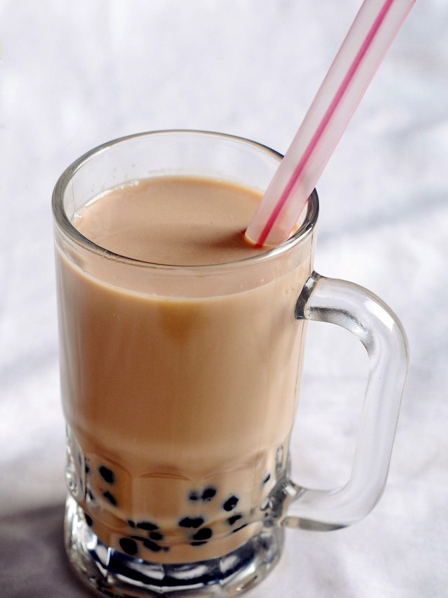 Classic bubble milk tea in a clear plastic cup with black tapioca pearls and a wide straw
