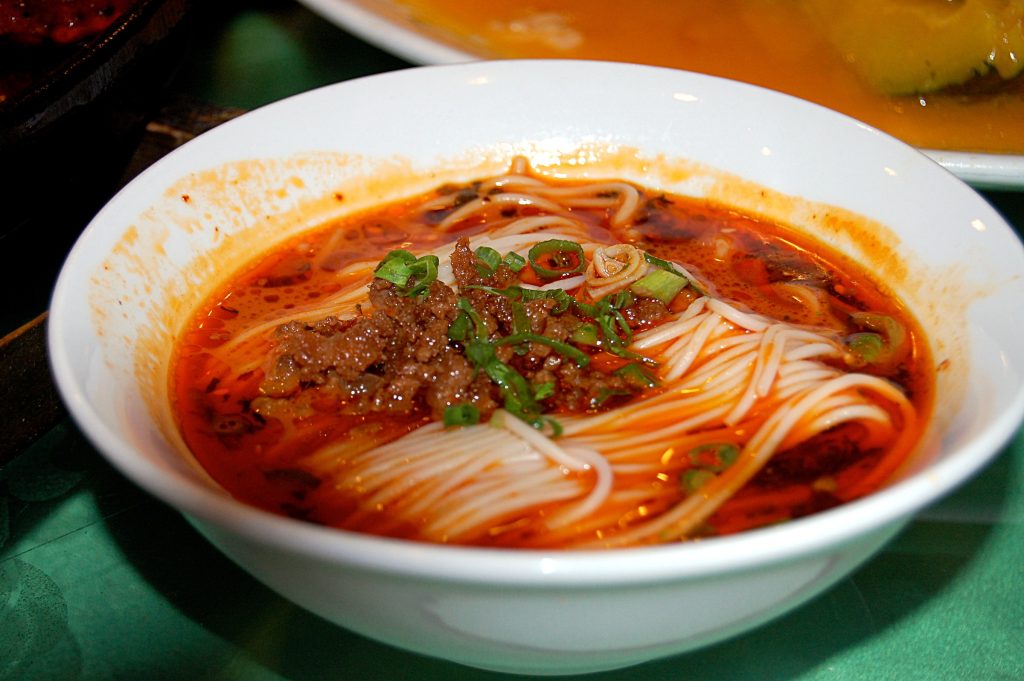 Bowl of dan dan noodles topped with minced meat sauce and chopped greens