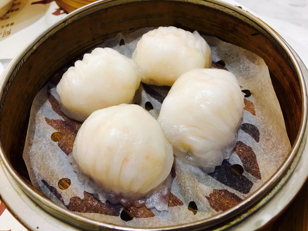 Bamboo steamer of translucent har gow shrimp dumplings on a restaurant table