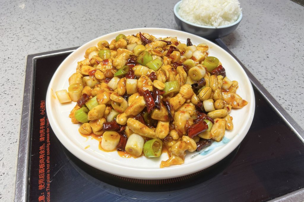 Sichuan-style Kung Pao chicken (gongbao jiding) with diced chicken, dried chilies, and peanuts on a restaurant plate