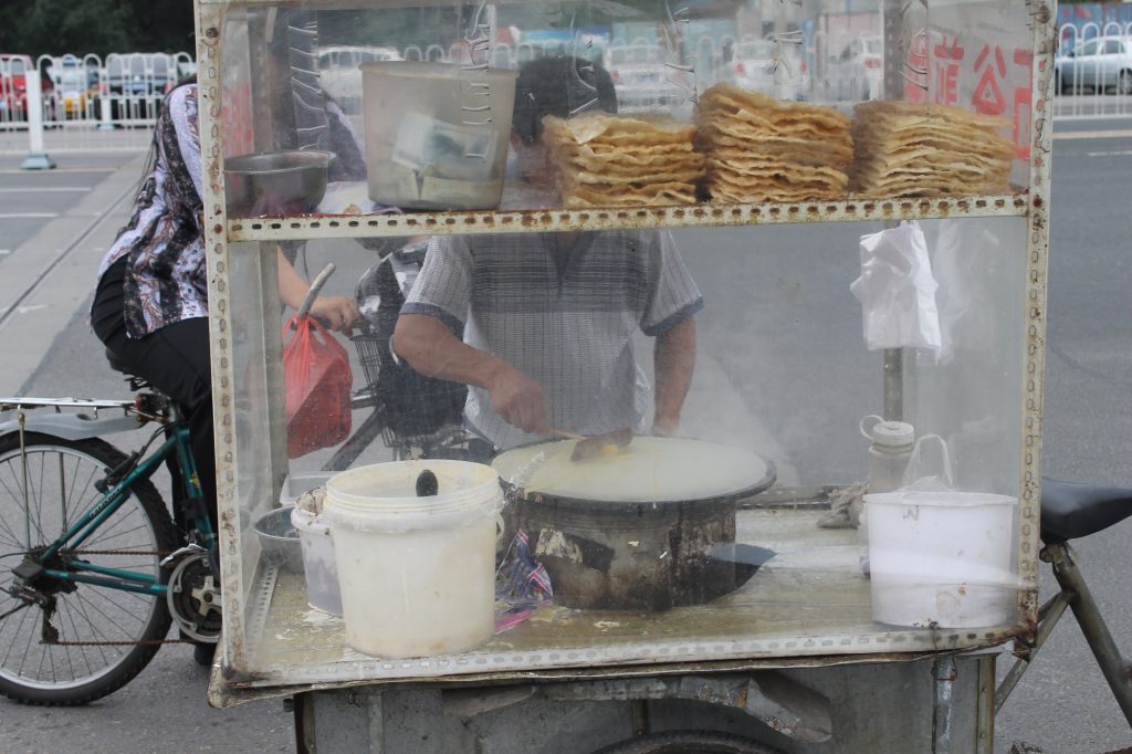 Street vendor spreading egg on a jianbing crepe cooking on a round griddle