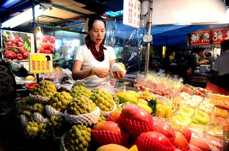 Vendor preparing tropical fruit at a brightly lit Taiwan night market stall