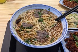 Bowl of Lanzhou-style beef noodle soup with clear broth, radish, chili oil, herbs, and yellow noodles