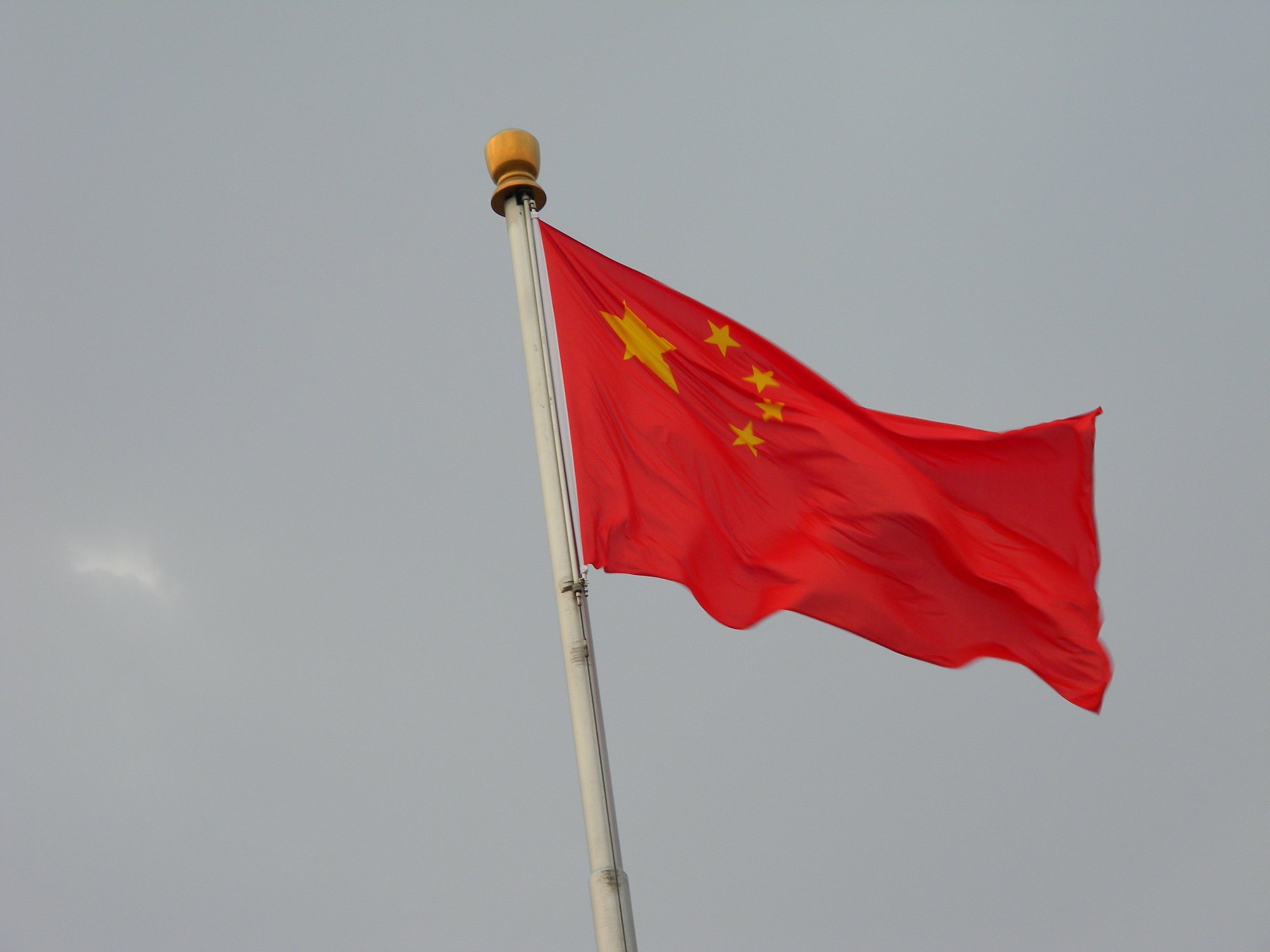 Chinese national flag flying against blue sky at Tiananmen Square in Beijing