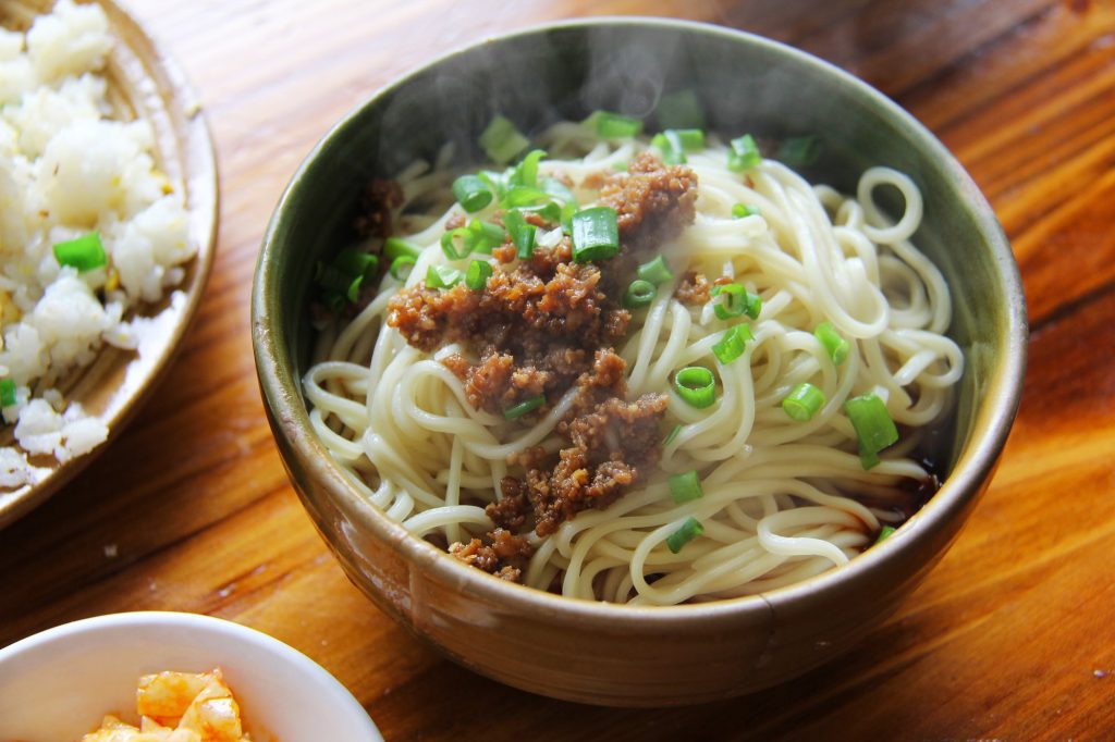Bowl of Sichuan dan dan noodles with minced pork, chili oil, and chopped toppings