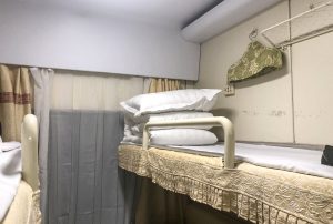 Upper berth inside a China Railway soft sleeper (RW25T) compartment with blue bedding and curtains