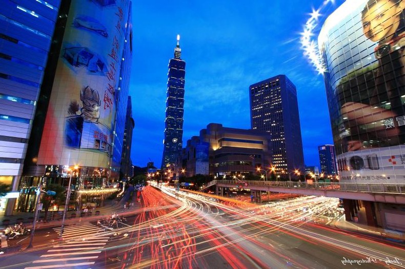 Taipei 101 glowing above Xinyi District traffic light trails at twilight